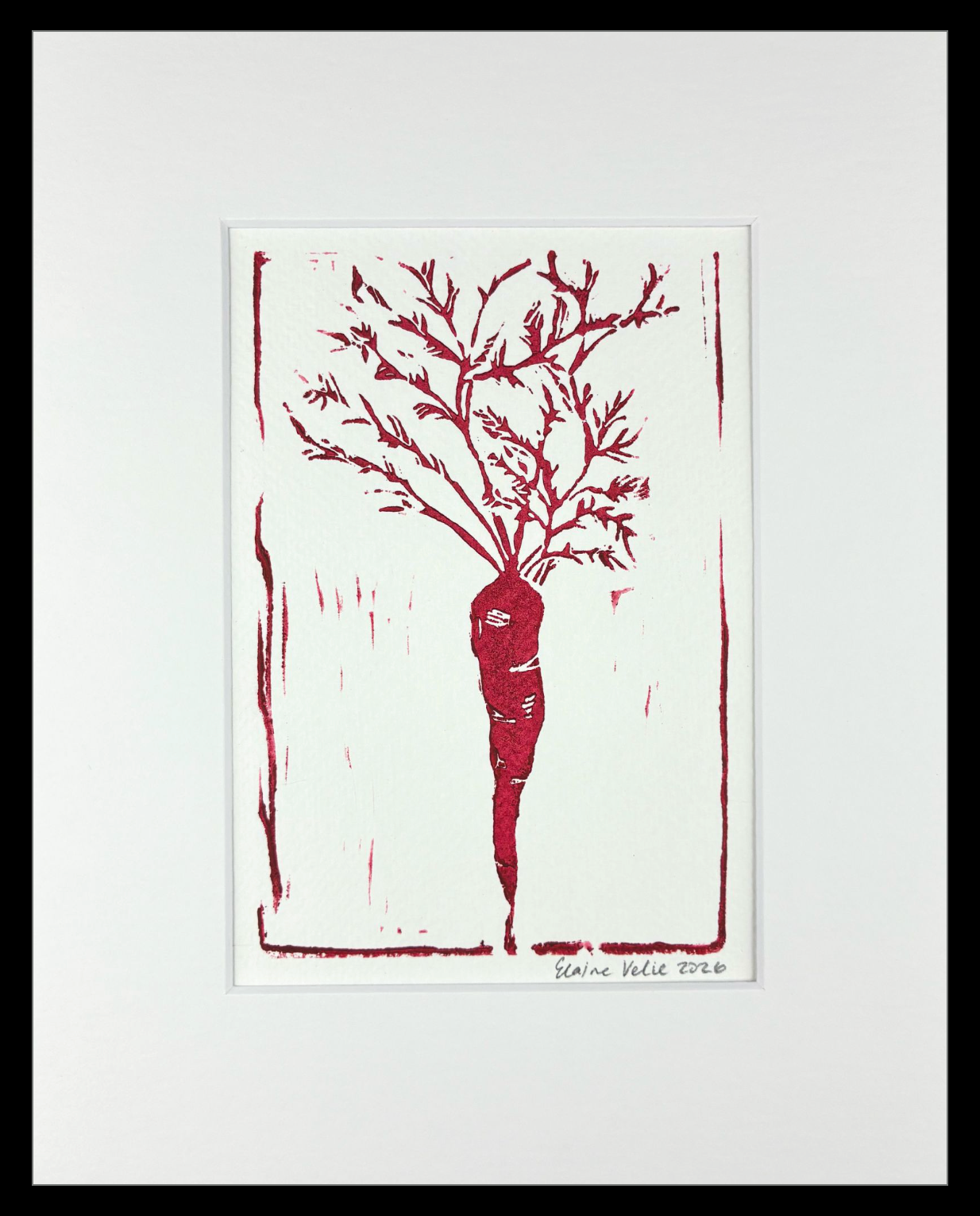 A framed art print featuring a red linocut-style illustration of a carrot with leafy roots on a white background, surrounded by a wide white mat and a black frame.