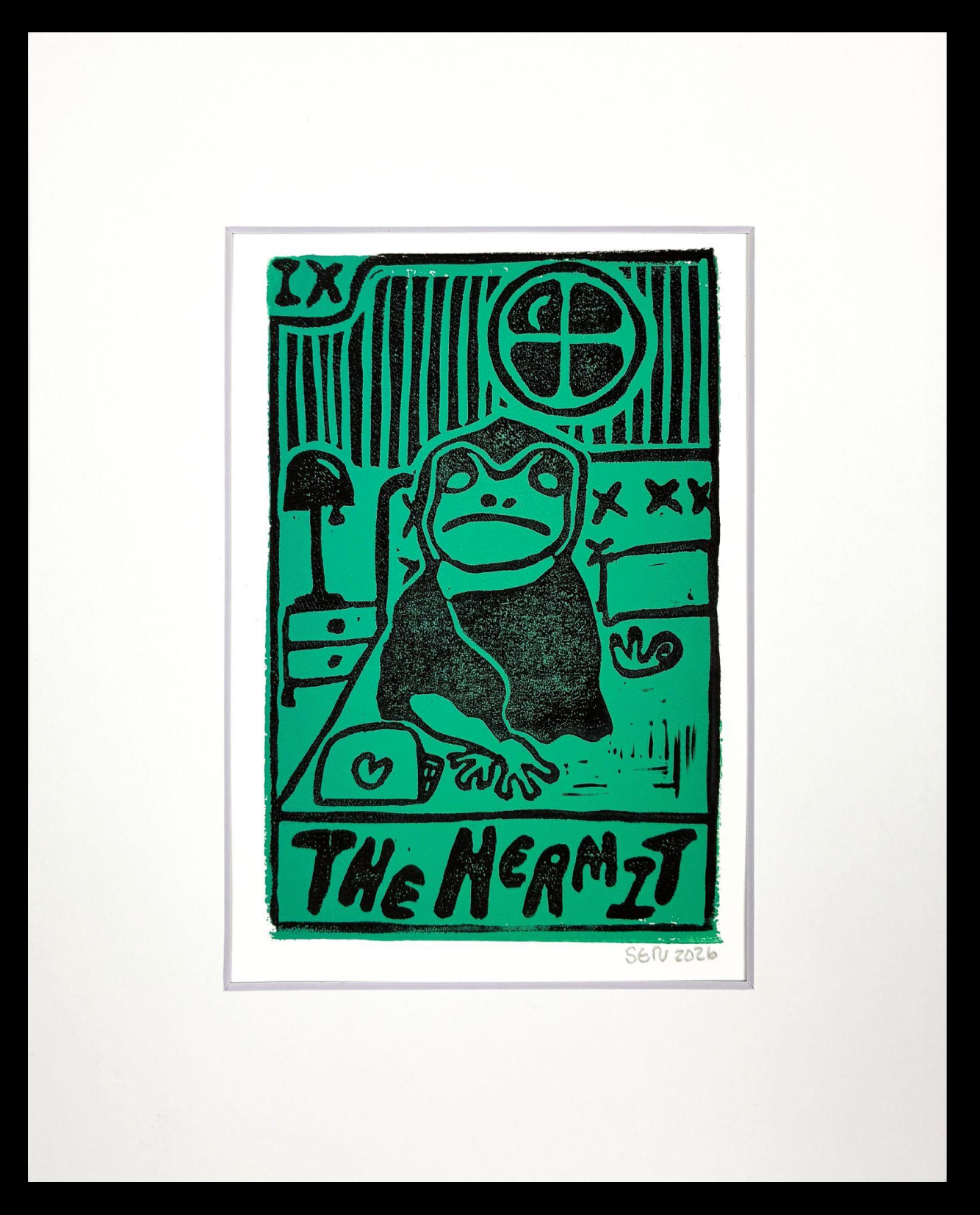 A matted green and black print showing a frog in a robe and the words The Hermit.